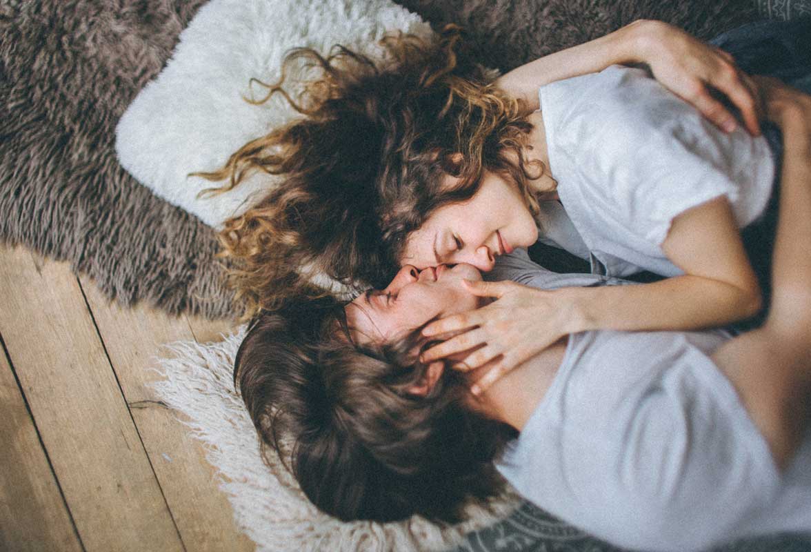 Les styles d’attachement : comprendre ta façon d’aimer Couple romantique étreignant et s'embrassant tendrement, allongé sur des tapis moelleux et des peaux de mouton. Scène intime et chaleureuse de deux personnes enlacées