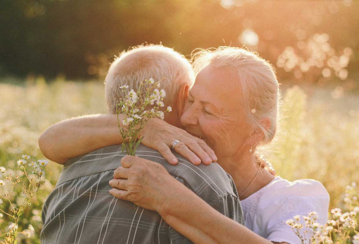 intelligence émotionnelle Couple de personnes âgées s'étreignant tendrement dans un champ de fleurs sous une lumière chaude de coucher de soleil. Représente l'amour, l'affection et le bonheur durable.