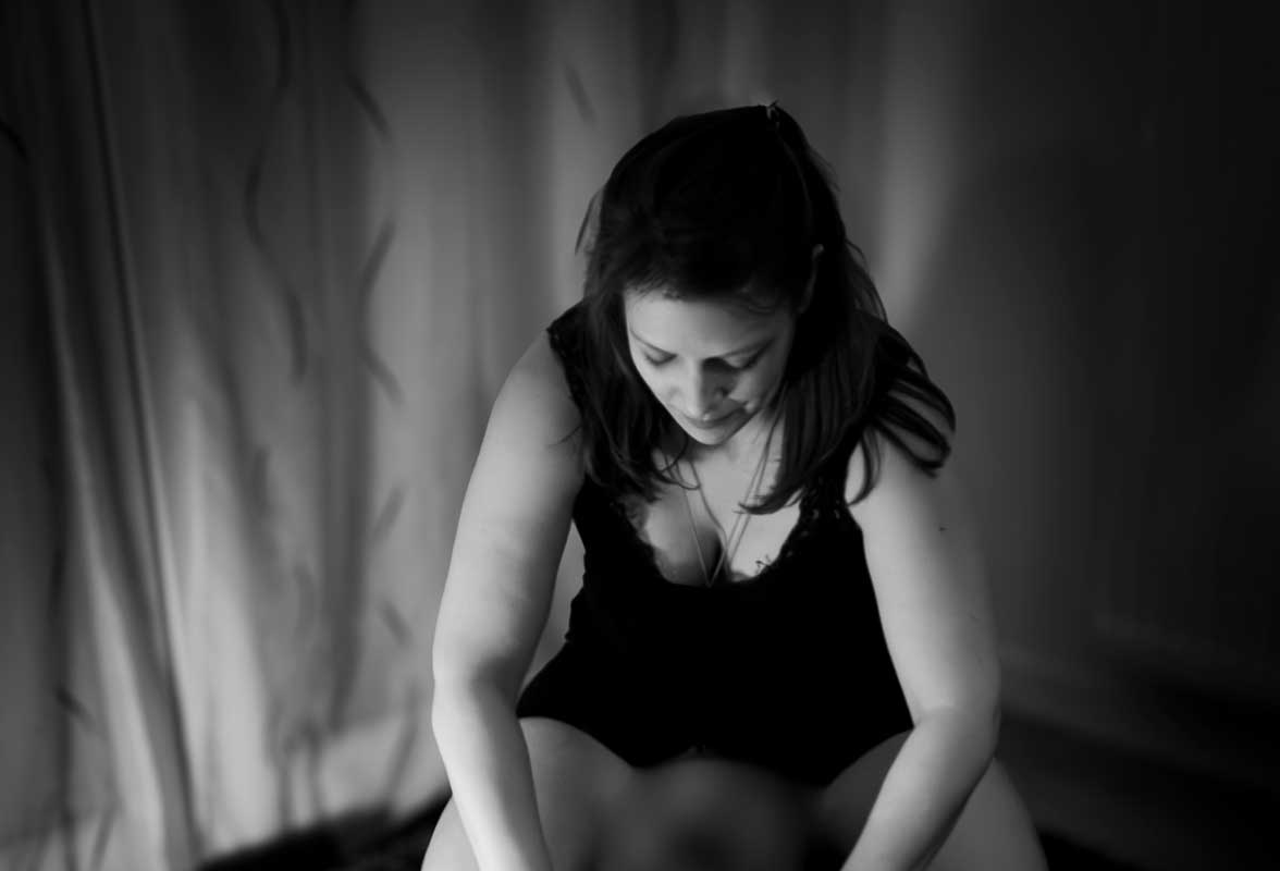 Femme concentrée en noir et blanc pratiquant un massage tantra sur une femme allongée. Elle est penchée en avant, vêtue de noir, dans une ambiance intime et tamisée.